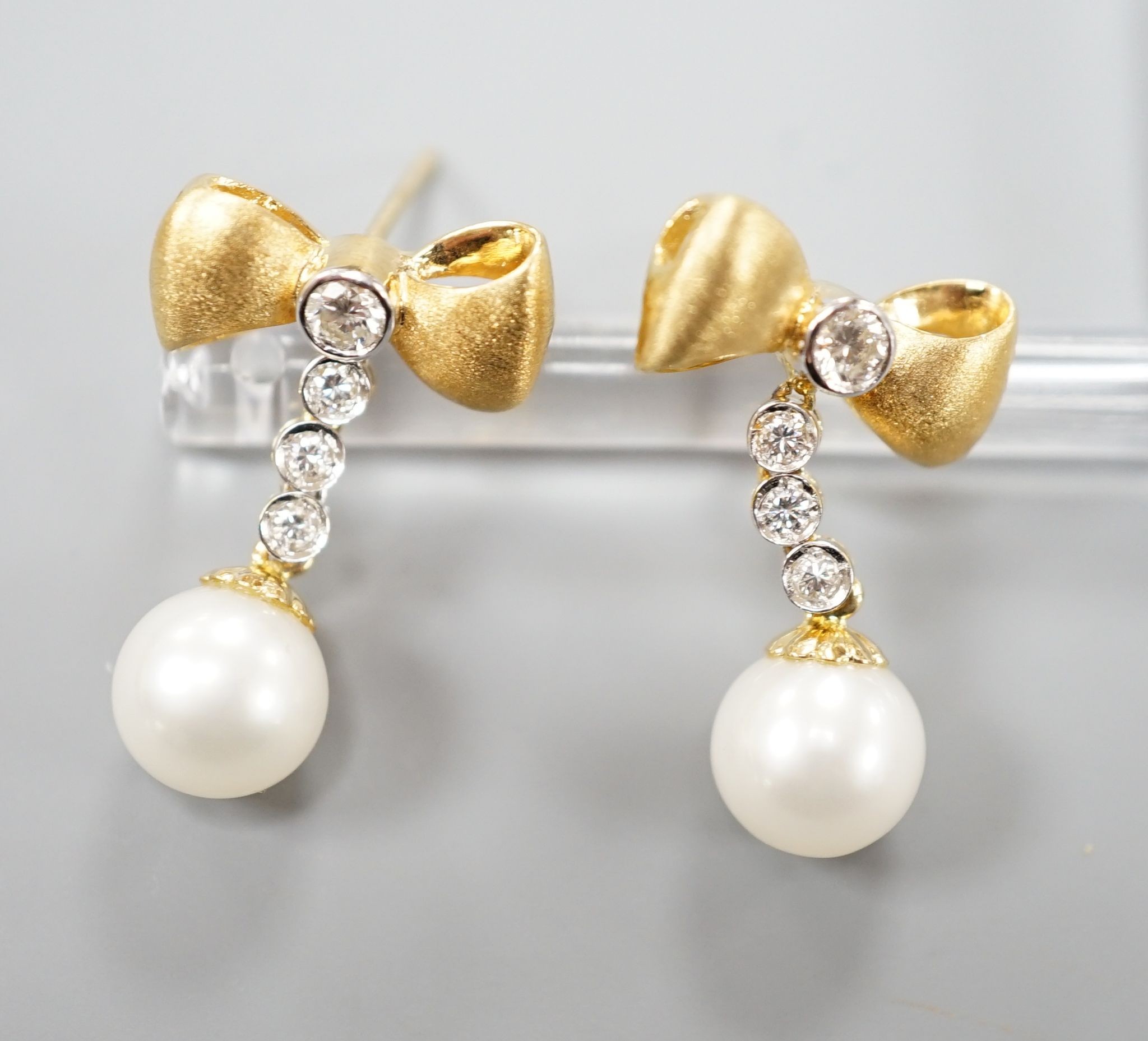 A modern pair of 750 yellow metal, cultured pearl and diamond set ribbon bow drop earrings